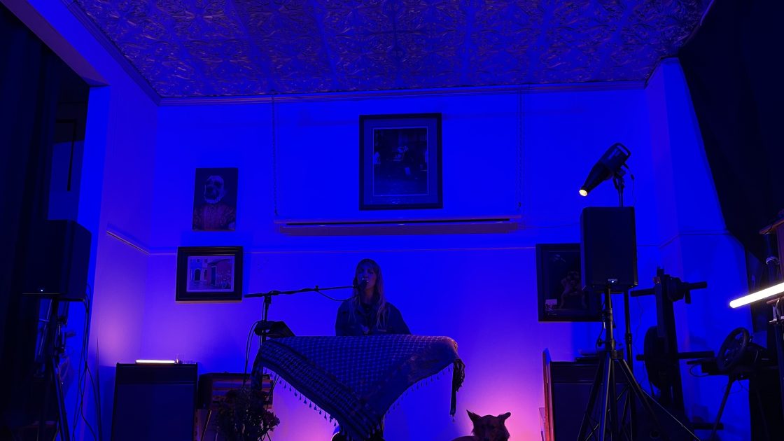 Laura Burhenn of The Mynabirds plays the keyboard and sings at an Undertow Show. Her dog, Eero, lays by her side.